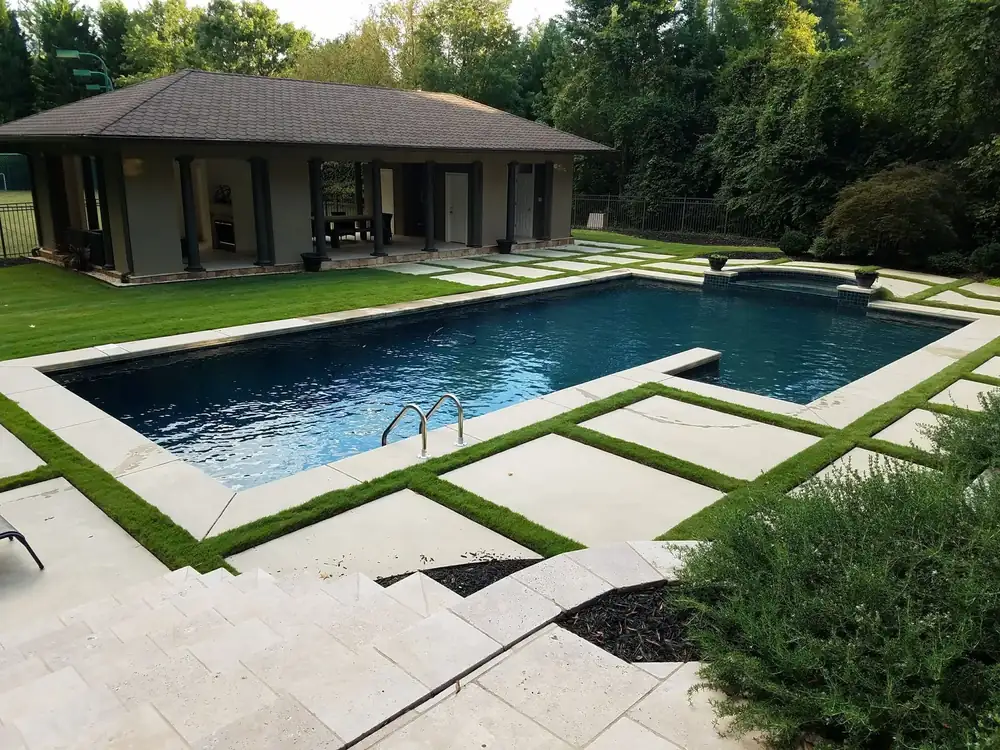 A pool and spa with a stone patio and pool house